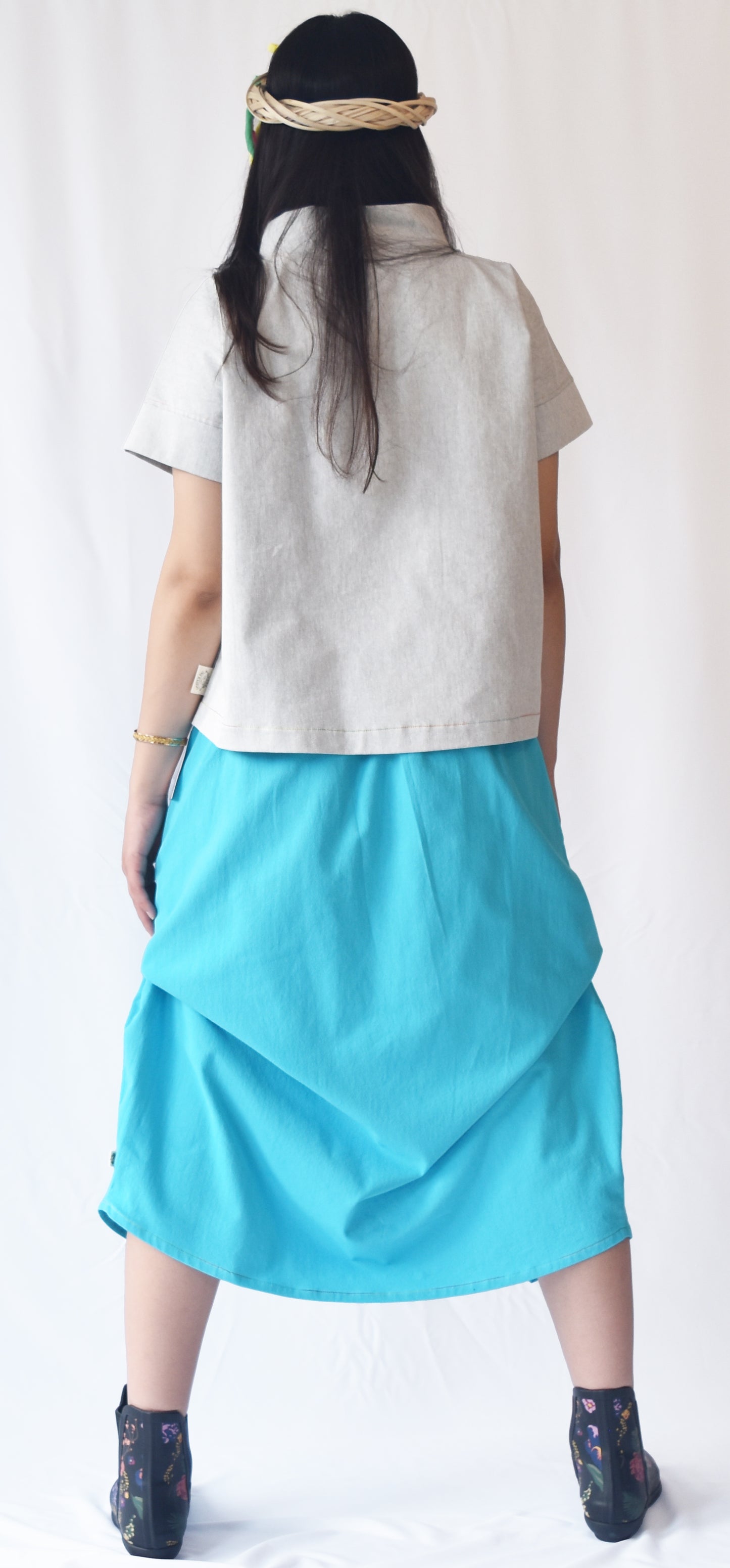 Woman wearing a blue wrap-style midi skirt with grey top and printed ankle boots. The SheKnows Brand skirt features an adjustable drape and midi length.