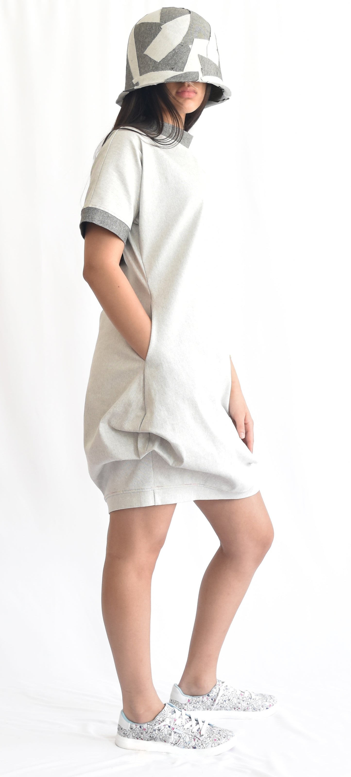 Woman wearing a short off-white denim dress with contrast grey stand collar and cuffs on short sleeves. The SheKnows Brand dress has pockets and a structured and playful silhouette