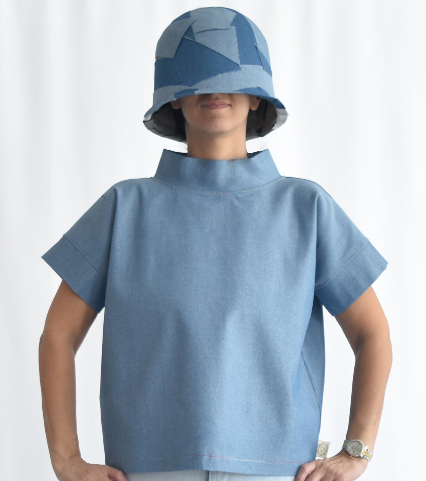 Woman wearing a light blue short-sleeve stretchy denim top with stand collar. The SheKnows Brand top has a structured, minimalist silhouette