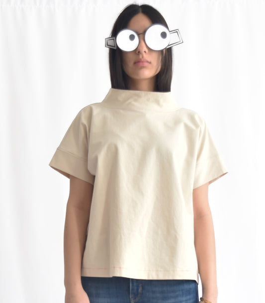 Woman wearing a minimalist cotton top with short sleeves and stand collar in birch from SheKnows Brand. The top has a high-hip length and relaxed fit.