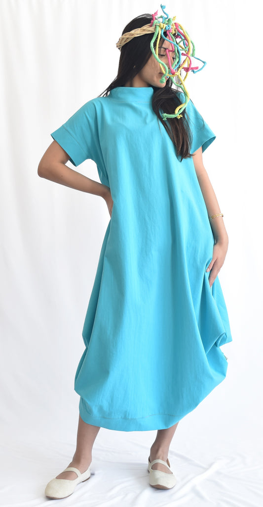 Woman wearing a blue loose-fit midi dress with short sleeves and pockets, made from cotton poplin fabric from SheKnows Brand