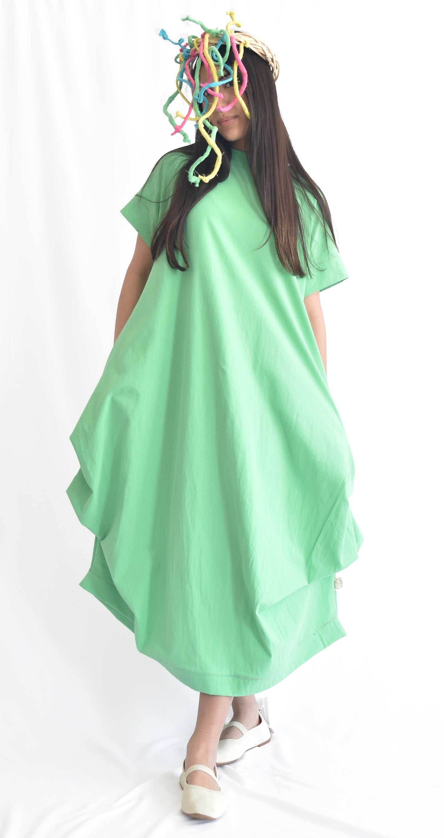 Woman wearing a green loose-fit midi dress with short sleeves and pockets, made from cotton poplin fabric from SheKnows Brand