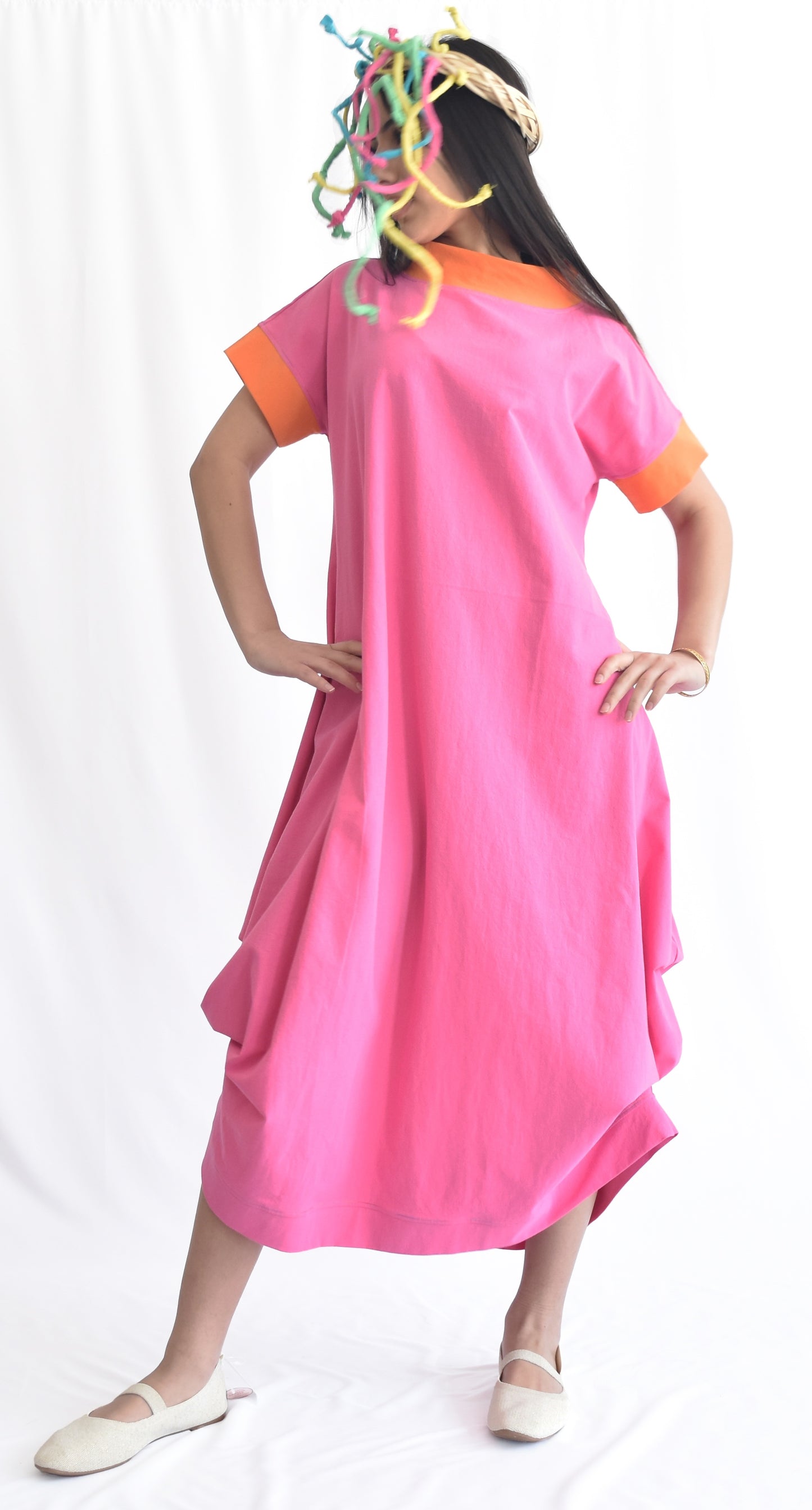 Woman wearing a pink loose-fit midi dress with short sleeves and pockets, made from cotton poplin fabric from SheKnows Brand