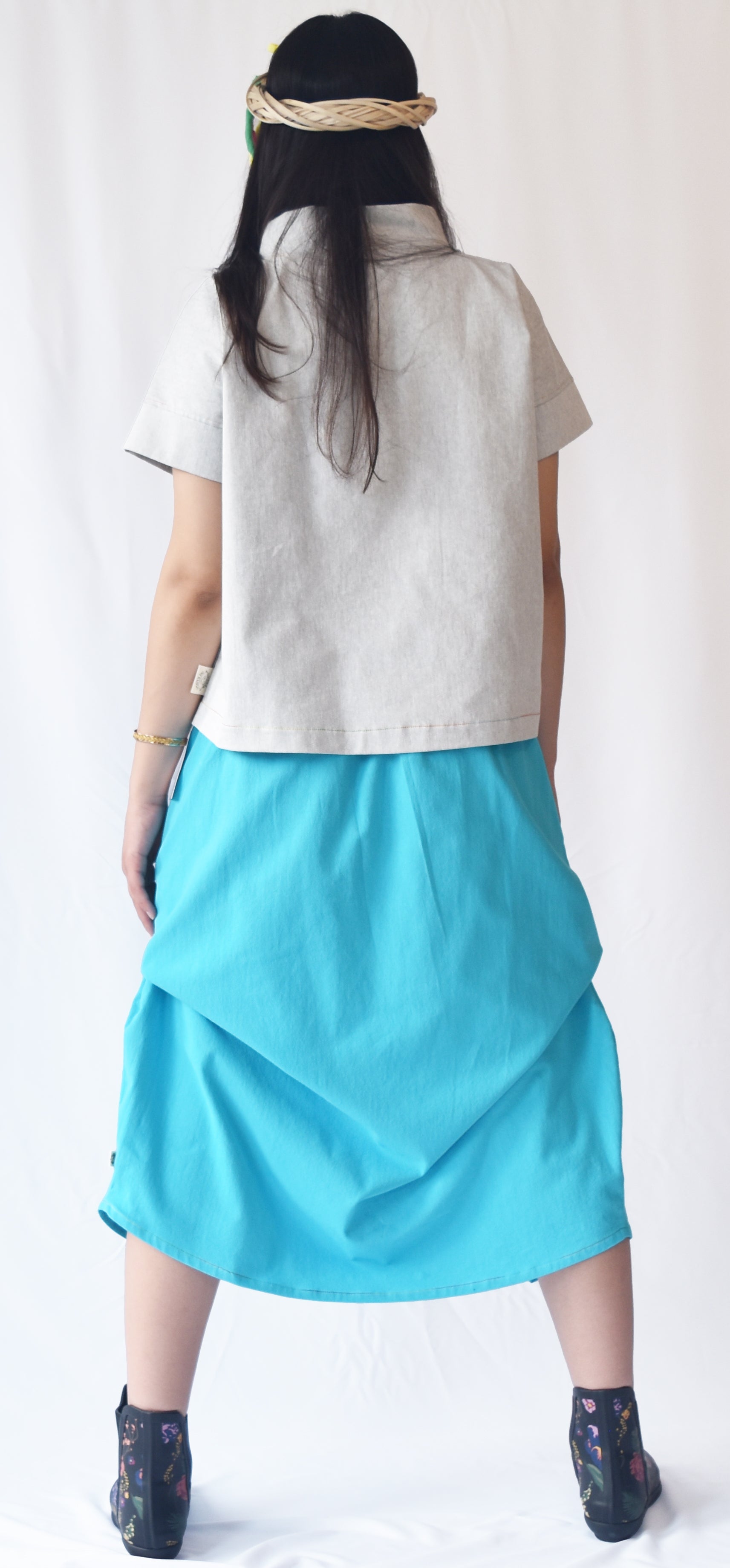 Woman wearing a blue wrap-style midi skirt with grey top and printed ankle boots. The SheKnows Brand skirt features an adjustable drape and midi length.
