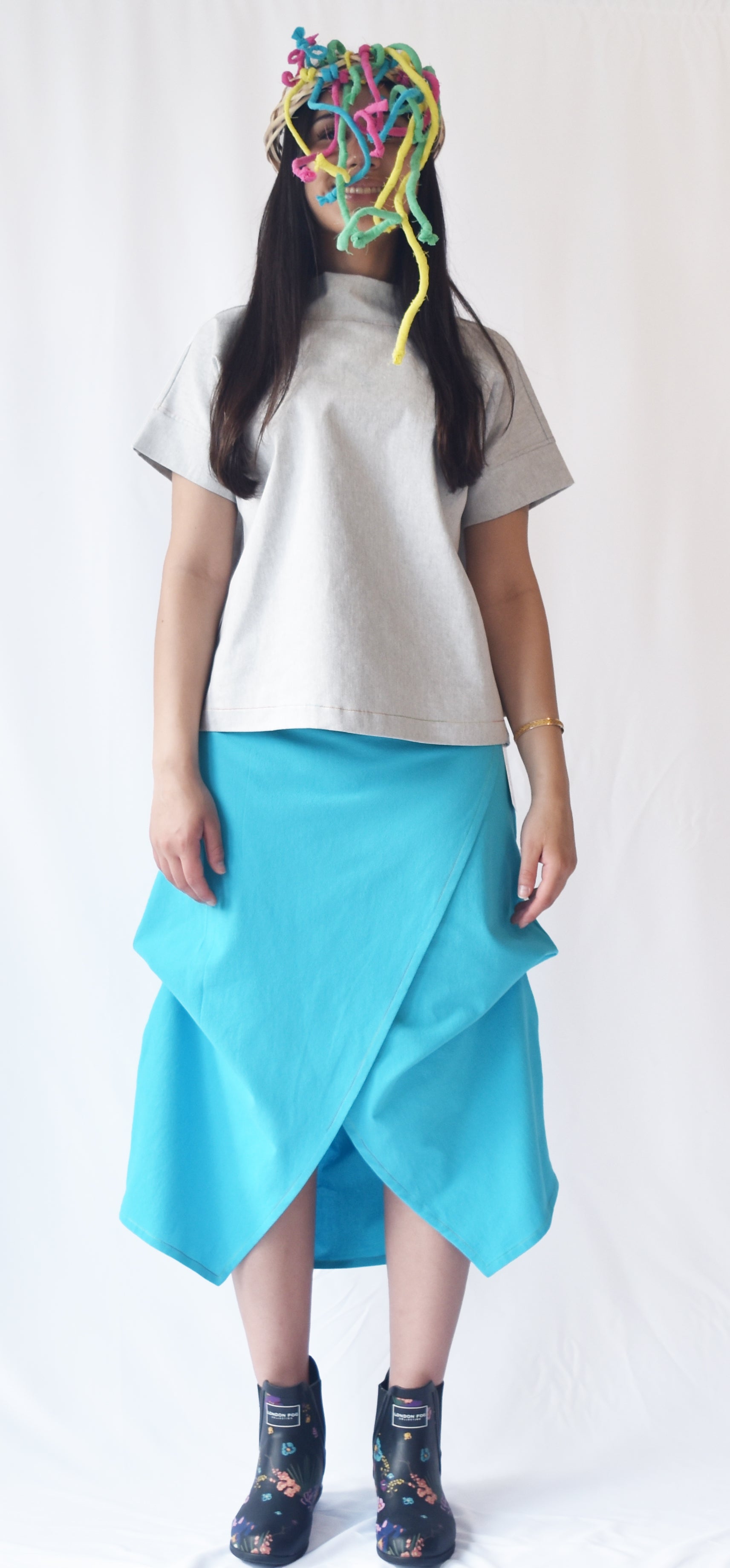 Woman wearing a blue wrap-style midi skirt with grey top and printed ankle boots. The skirt features an adjustable drape and midi length.