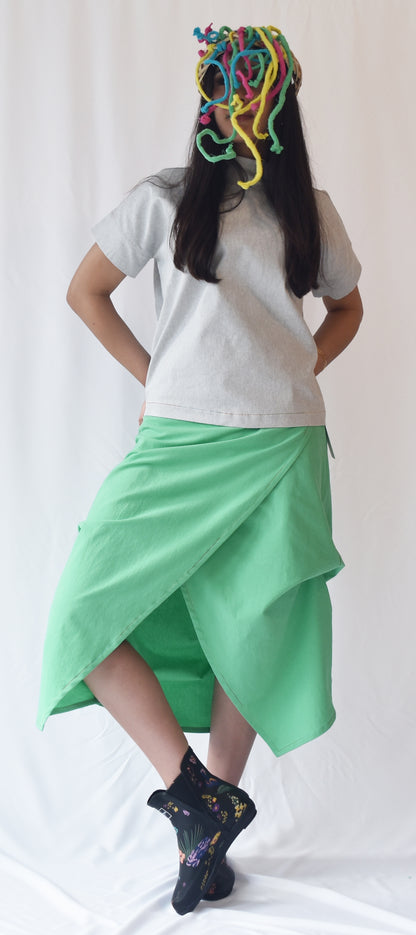Woman wearing a green wrap-style midi skirt with grey top and printed ankle boots. The SheKnows Brand skirt features an adjustable drape and midi length.