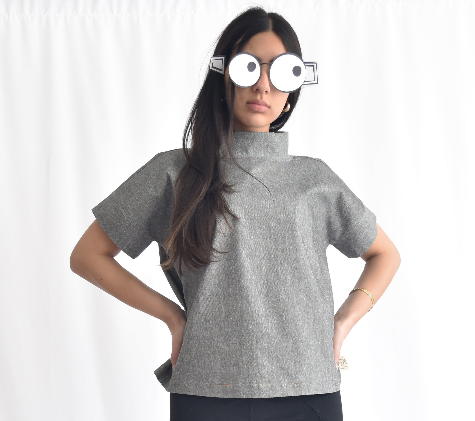 Woman wearing a grey short-sleeve stretchy denim top with stand collar. The SheKnows Brand top has a structured, minimalist silhouette