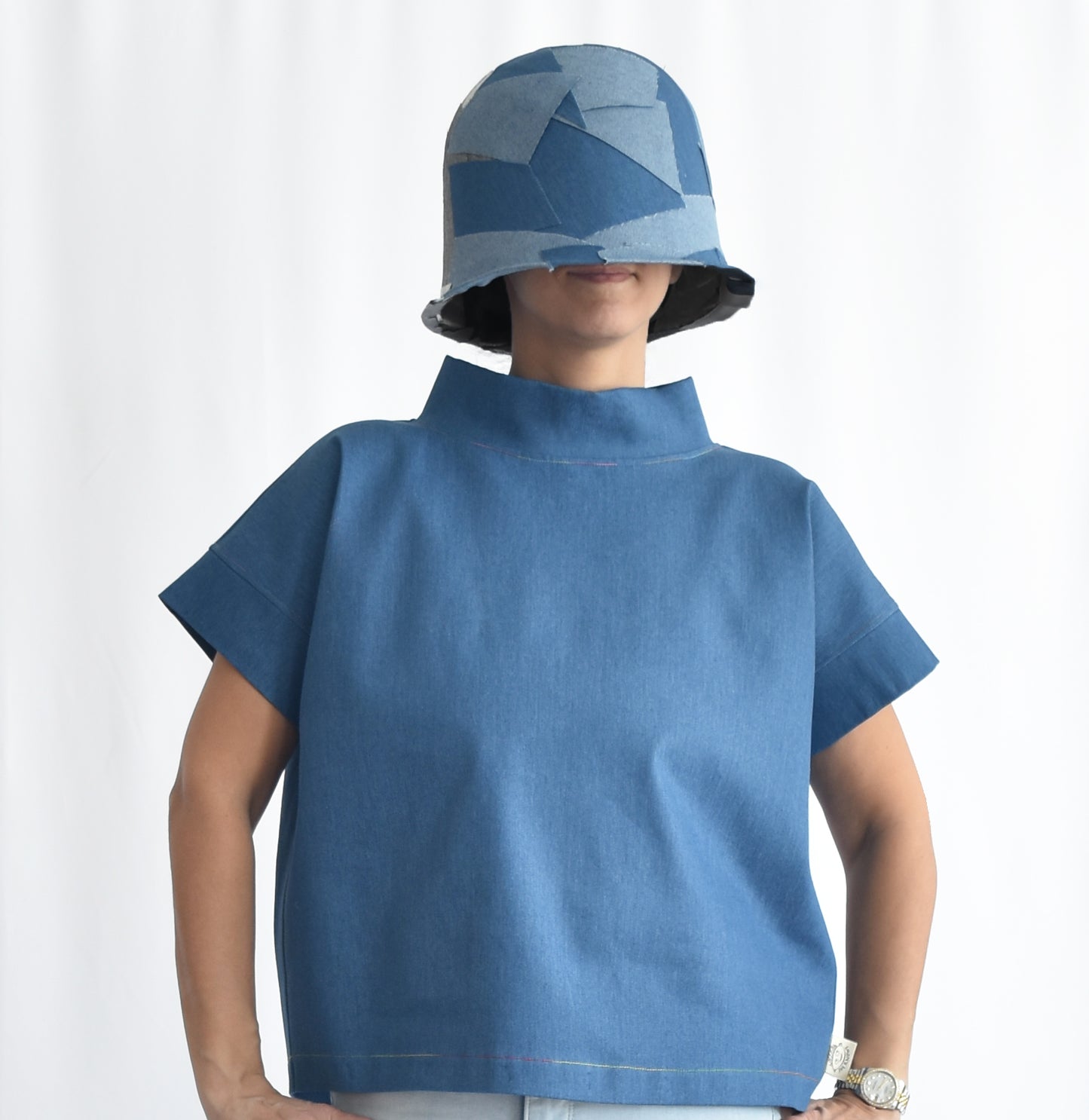 Woman wearing a medium blue short-sleeve stretchy denim top with stand collar. The SheKnows Brand top has a structured, minimalist silhouette