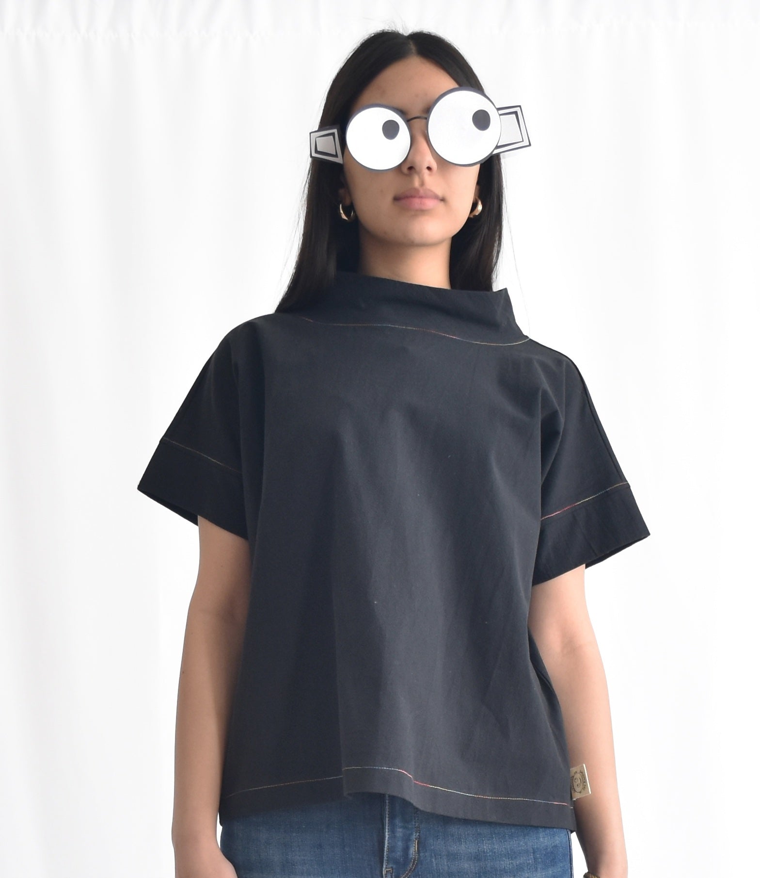 Woman wearing a minimalist cotton top with short sleeves and stand collar in black from SheKnows Brand. The top has a high-hip length and relaxed fit.