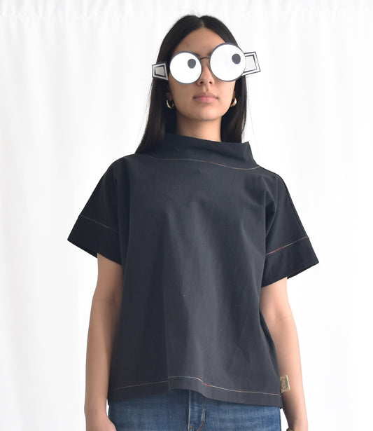 Woman wearing a minimalist cotton top with short sleeves and stand collar in black from SheKnows Brand. The top has a high-hip length and relaxed fit.