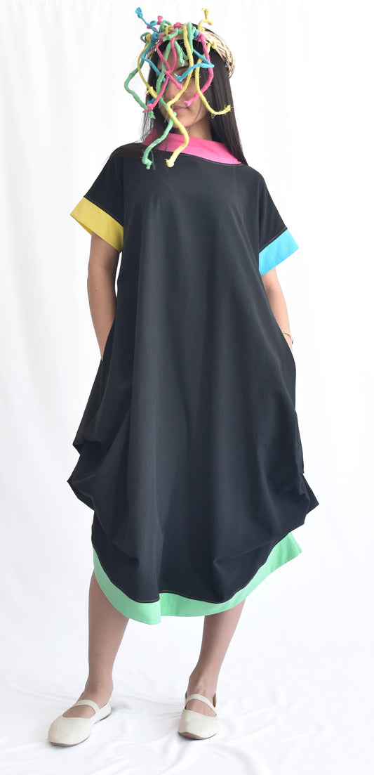 Woman wearing a black loose-fit midi dress with short sleeves and pockets, made from cotton poplin fabric with popping colors as details from SheKnows Brand